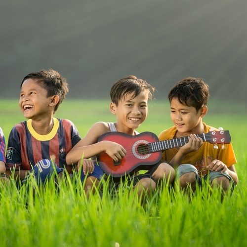 A group of children sitting in a field and playing a guitar.